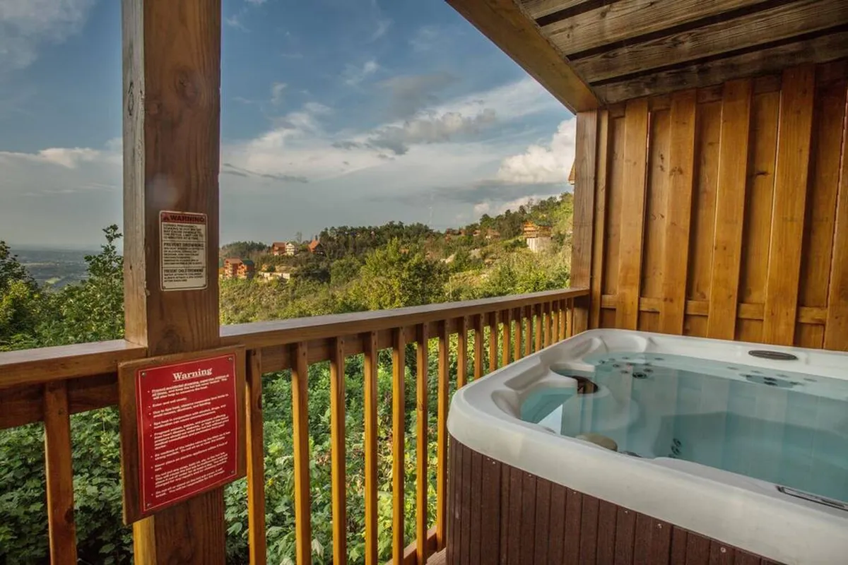 An outdoor hot tub set on a wooden deck, overlooking a scenic natural view. The setting is serene, perfect for relaxing soaks while watching the sunset or stars, embodying the ultimate mountain retreat experience.