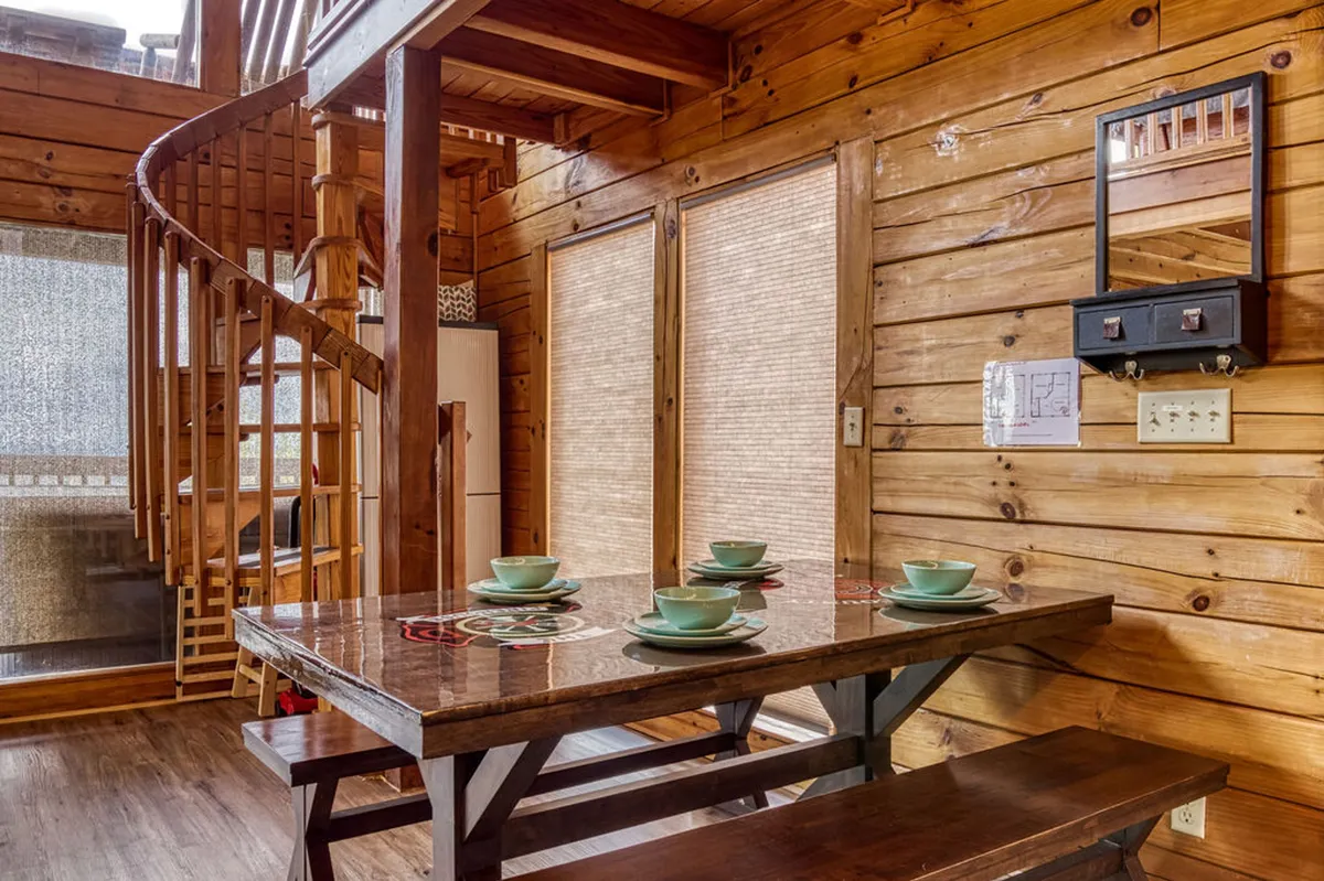 A cozy interior shot featuring a dining table with place settings, a striking spiral staircase, and warm wooden walls. The setting is intimate and perfect for stories and laughter shared over a meal, with natural light enhancing the inviting atmosphere.
