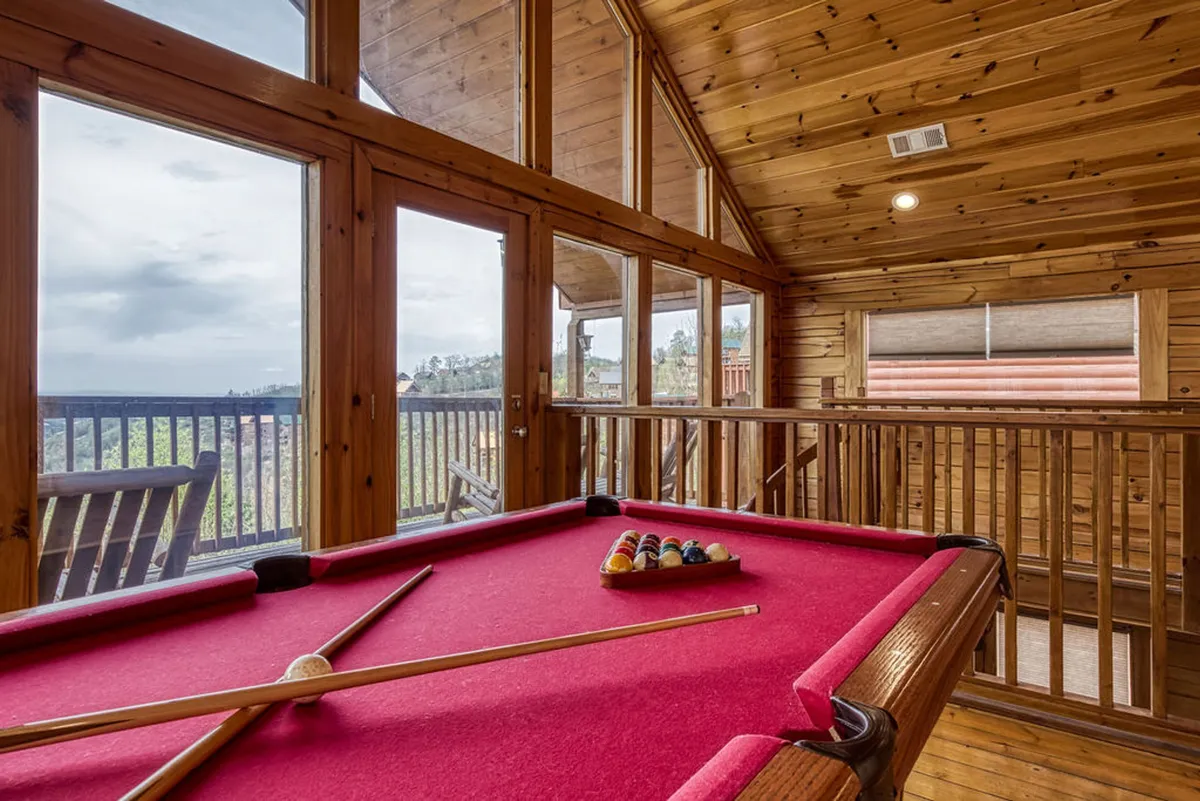 This interior image shows a well-lit game area featuring a pool table set against wooden walls and large windows that provide an inviting outdoor view. The open, recreational setting is ideal for socializing and enjoying classic games.