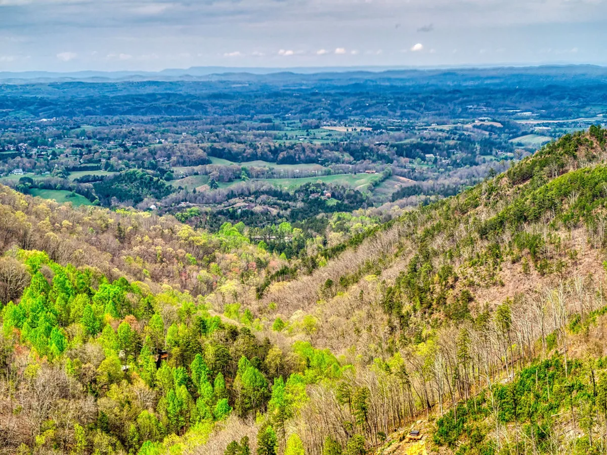 A sweeping view of lush green valleys, rolling hills, and distant mountains beneath a clear sky. The image evokes the grandeur and serenity of the Smokies, inviting guests to explore nature or simply soak in the view from their retreat.
