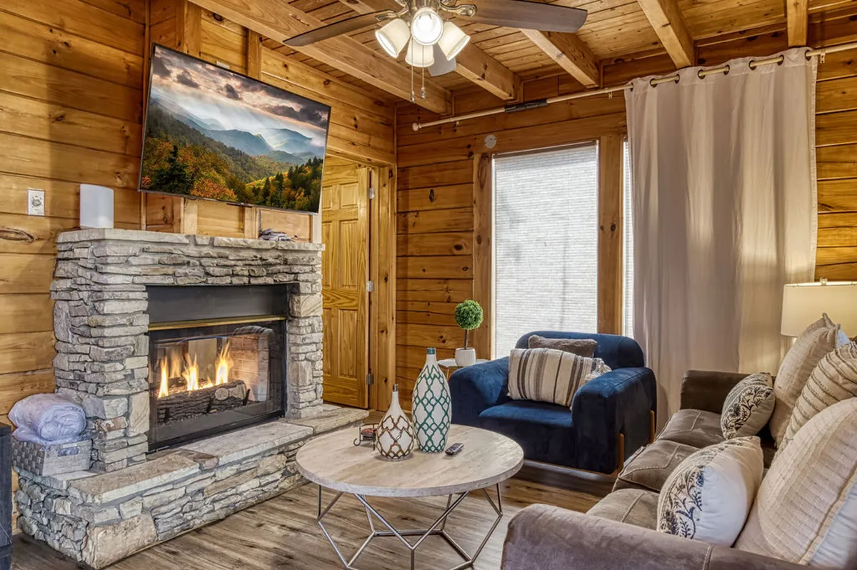 A welcoming living area featuring a stylish fireplace, a plush sofa, decorative vases, a coffee table, and a large TV. Light pours in from the windows, hinting at scenic views beyond, while the overall setup invites groups to relax and spend time together.