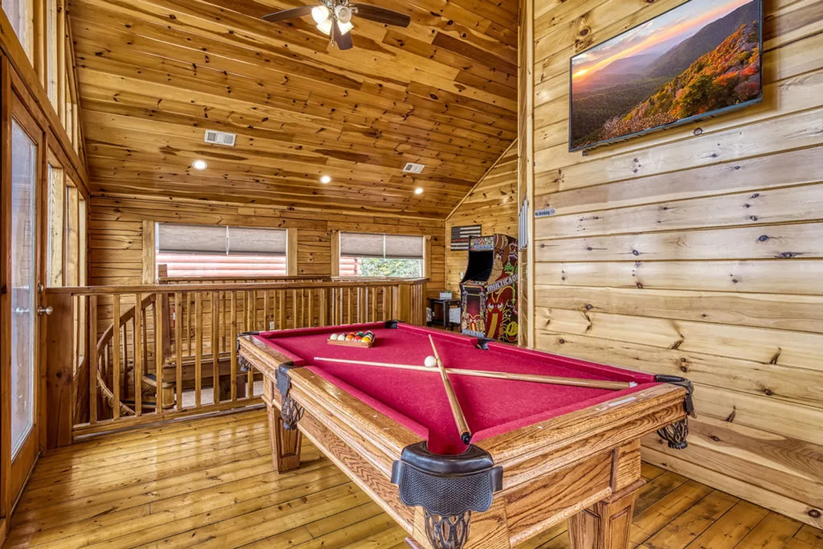A spacious entertainment area with a pool table, wood-paneled walls, large windows, and a television, creating a lively and relaxed space for group gatherings and game nights.