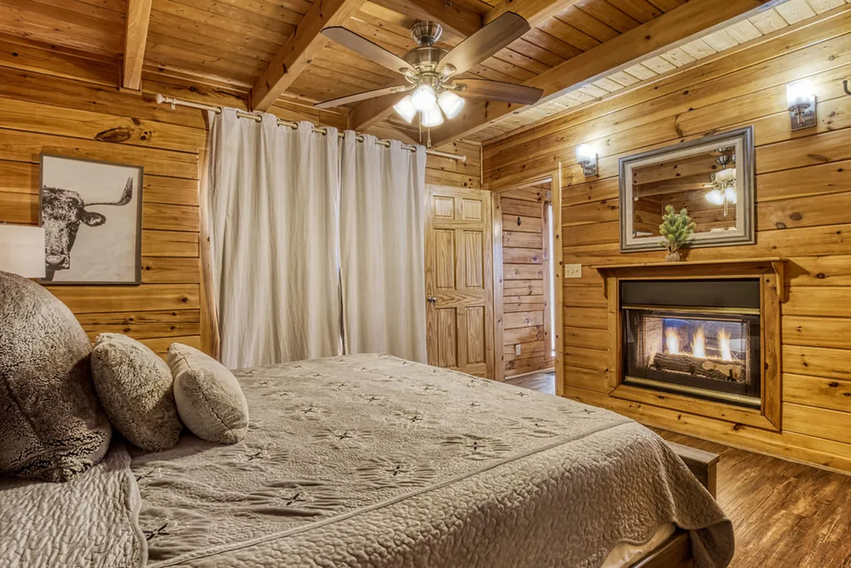 A cozy bedroom featuring a bed positioned beside a fireplace, with tasteful artwork above. The warm glow of the fireplace creates an inviting, luxurious atmosphere ideal for unwinding in comfort.